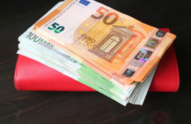 Pila de billetes en euros en monedero rojo sobre fondo de madera negra
