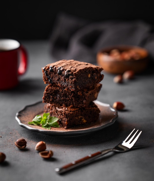 Una pila de brownies de chocolate con menta y avellanas sobre un fondo oscuro con una taza de café y nueces