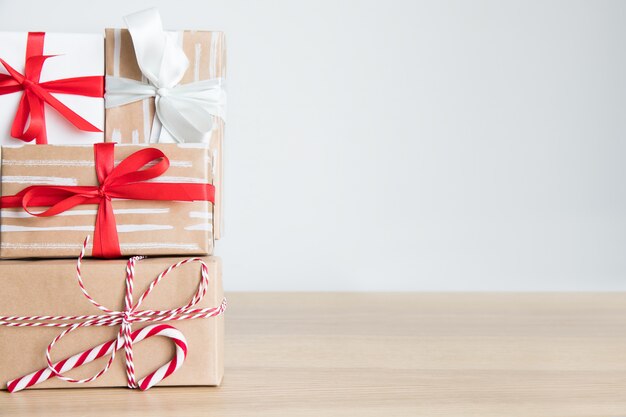 Pila de cajas de regalos de Navidad en papel artesanal con cinta roja, blanca, bastones de caramelo sobre la mesa. Fondo blanco, espacio libre.