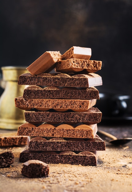 Pila de chocolate amargo y con leche aireado poroso y cacao en una mesa oscura. Surtido de diferentes tipos de chocolate. Enfoque selectivo.