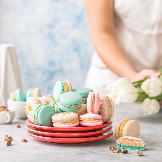 Pila de coloridos macarons franceses o italianos en placa roja. Postre para servir con té de la tarde o pausa para el café. Fondo de comida hermosa con mano de mujer