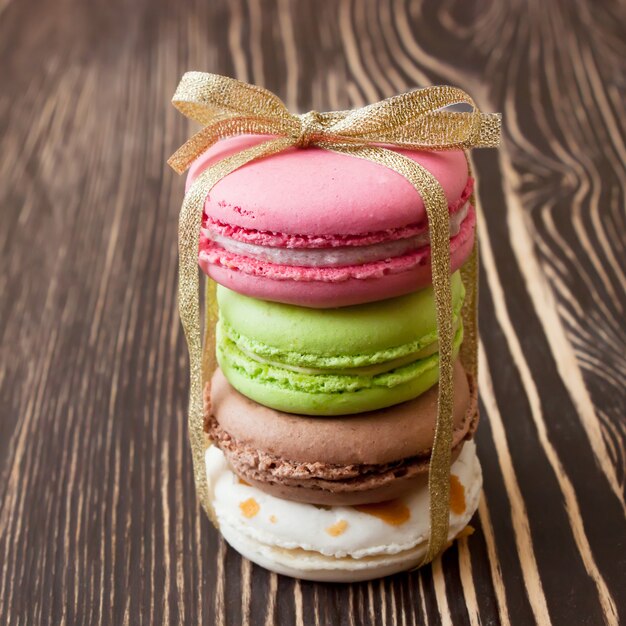 Una pila de coloridos makarons de postre francés tradicional con lazo dorado sobre fondo de madera marrón.