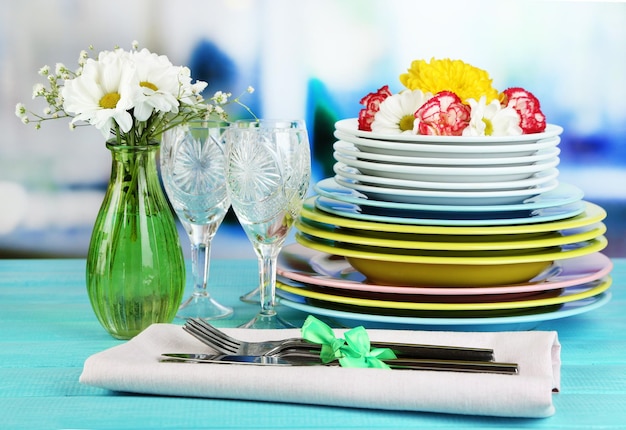 Pila de coloridos platos de cerámica y flores sobre una mesa de madera sobre un fondo claro