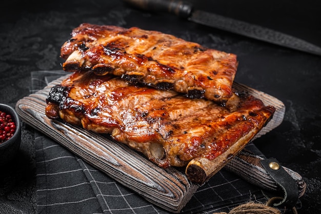 Foto pila de costillas de cerdo a la parrilla en salsa barbacoa en una tabla de cortar fondo negro vista superior