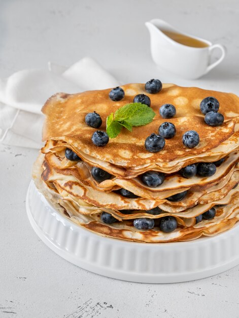 Pila de crepes con arándanos frescos sobre fondo blanco.