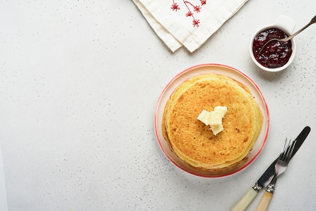 Pila de crepes o panqueques finos con mantequilla y mermelada de frambuesa en un hermoso plato de cerámica