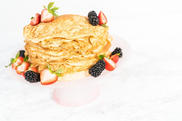 Pila de crepes recién horneados con bayas en un puesto de pasteles.