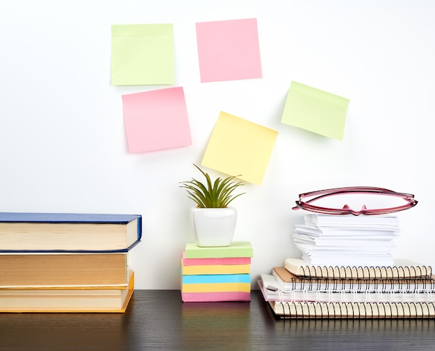 Pila de cuadernos de espiral y pegatinas de colores, junto a una maceta de cerámica con una flor.