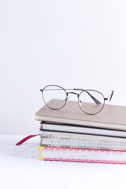 Pila de cuadernos para notas y anotaciones con gafas en la parte superior de una mesa blanca