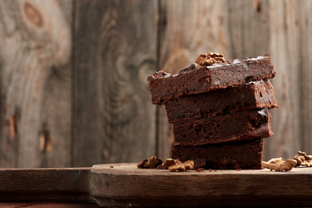 Pila de cuadrados al horno rebanadas de pastel de chocolate brownie con nueces sobre una superficie de madera. Comida casera cocinada