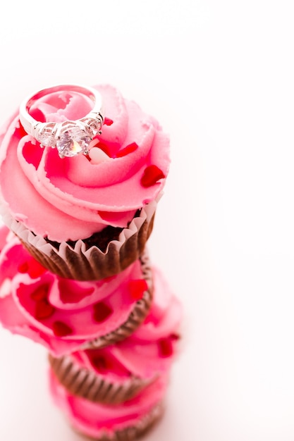 Pila de cupcakes rosas con anillo de compromiso en la parte superior.