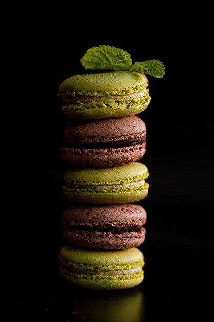 Foto pila decadente de cinco macarrones de chocolate y pistacho sobre fondo oscuro adornado con menta