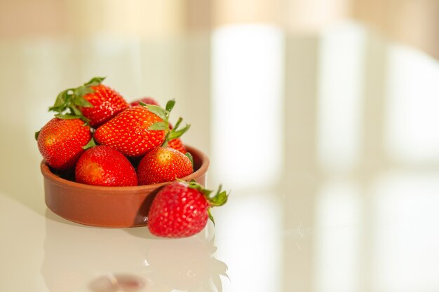 Pila de deliciosas fresas rojas con hojas en una placa de arcilla sobre una mesa de vidrio. Espacio vacio