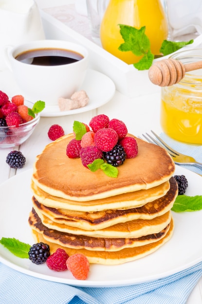 Pila de deliciosos panqueques americanos con bayas para el desayuno sobre un fondo blanco.