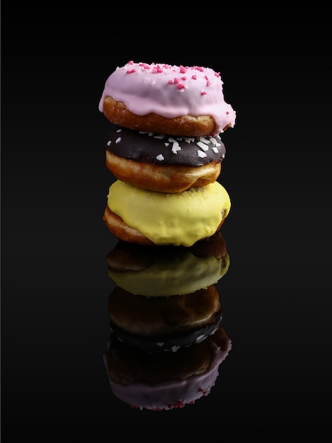 Una pila de donas con glaseado y chocolate en polvo, reflejado en el espejo. Sobre un fondo negro, aislar, copiar espacio.