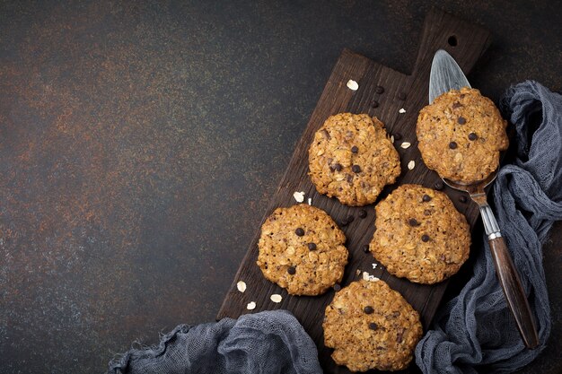 Pila de galletas de avena con chocolate y copos en piedra o hormigón oxidado oscuro.