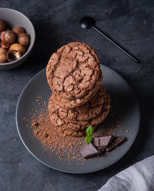 Una pila de galletas de chispas de chocolate con chispas de chocolate, nueces y hojas de menta sobre una mesa oscura. Vista superior y de cerca