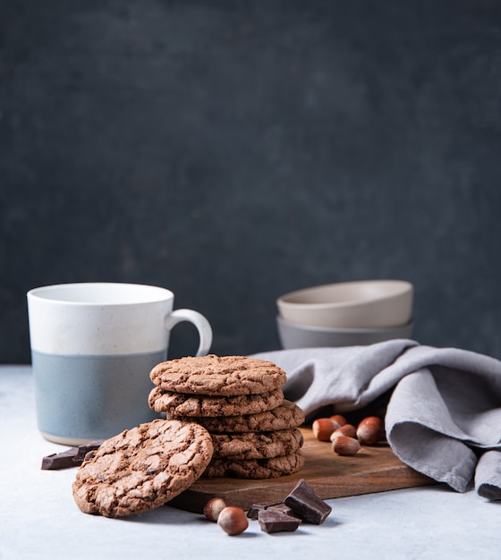 Una pila de galletas con chispas de chocolate con chispas de chocolate y nueces con una taza de té sobre una mesa de luz. Vista frontal y espacio de copia.