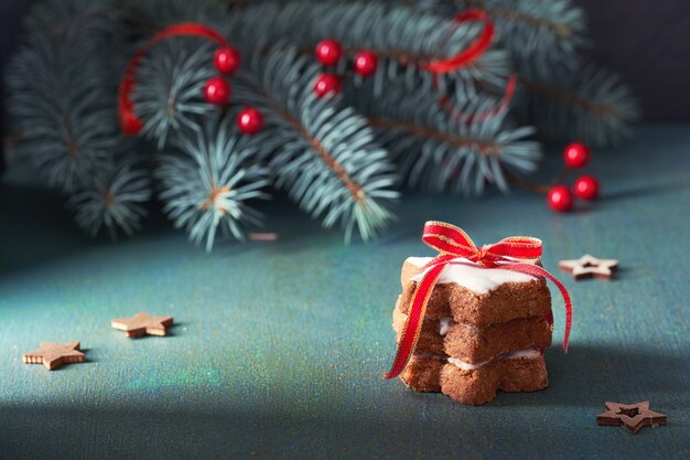 Pila de galletas estrella de Navidad atado con cinta médula roja sobre mesa festiva verde y roja con ramitas de abeto verde