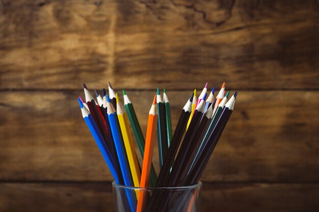 pila de lápices de colores en un vaso de vidrio sobre una madera