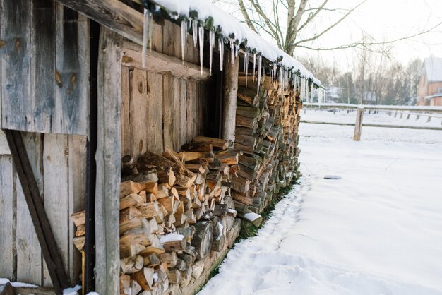 Pila de leña en las afueras de una granja, patio y bosque de invierno