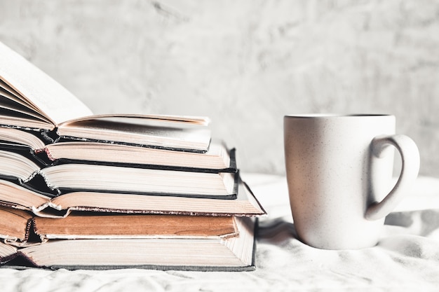 Pila de libros abiertos con una taza de café en la cama