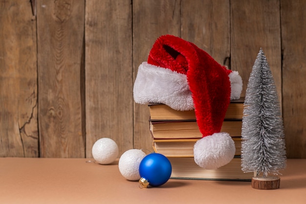 Pila de libros, adornos navideños y sombrero de Santa Claus sobre fondo de madera.