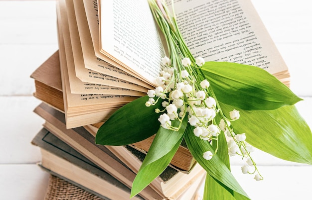 Una pila de libros antiguos y un ramo de lirios del valle de primavera en un libro abierto vista frontal composición de primavera con flores buenos días humor