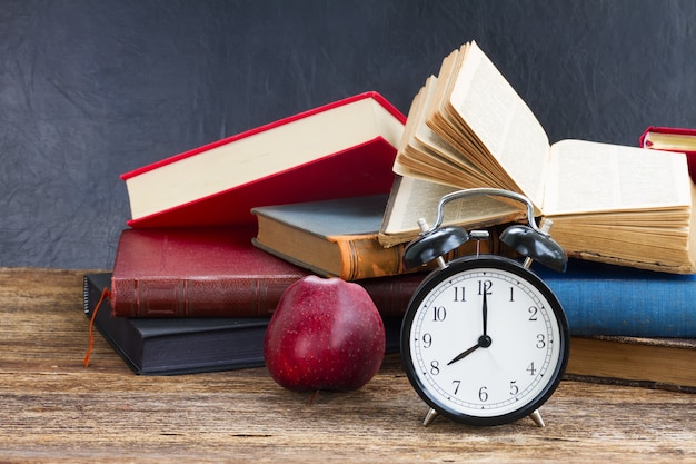 Pila de libros antiguos con reloj despertador antiguo y manzana en estante de madera