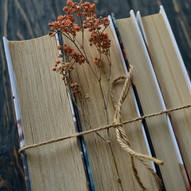Una pila de libros atados con hilo y flores secas en una vista superior de madera oscura. De cerca. Endecha plana.