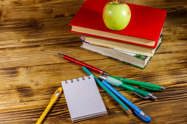 Pila de libros, bloc de notas, bolígrafos, lápices y manzana en el escritorio de madera Concepto de regreso a la escuela