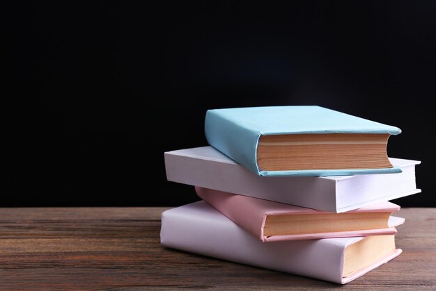 Pila de libros coloridos cerrados sobre una mesa de madera con fondo negro