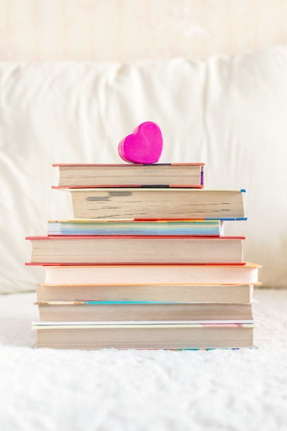 Pila de libros y corazón rosa en la cama blanca
