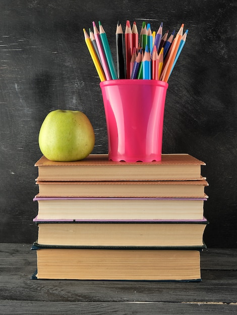 Pila de libros y un cristal de escritorio azul con lápices de madera multicolores