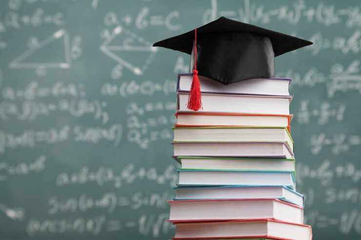 Foto pila de libros escolares con el clásico sombrero de graduación negro con la junta escolar