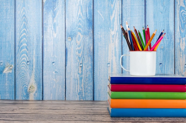 Pila de libros con espinas de colores, lápices de colores en una taza y espacio de copia