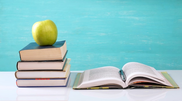 Una pila de libros, un libro abierto, una manzana verde sobre la mesa.