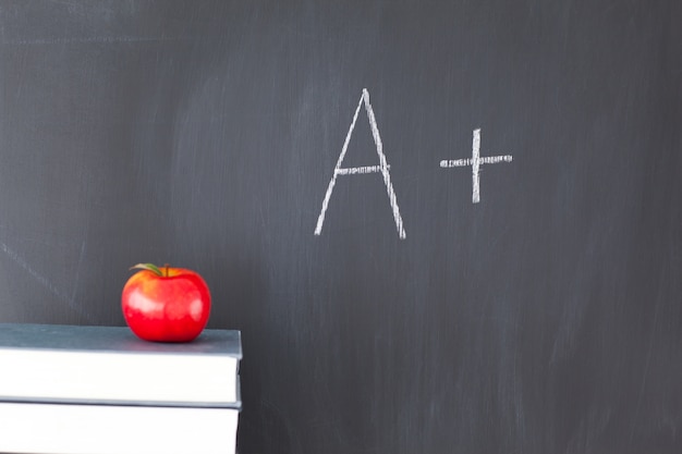 Pila de libros con una manzana roja y una pizarra con &quot;A +&quot; escrito en ella