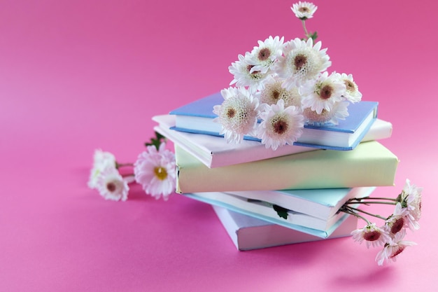 Una pila de libros con marcadores de flores de crisantemo frescas, sobre un fondo rosa