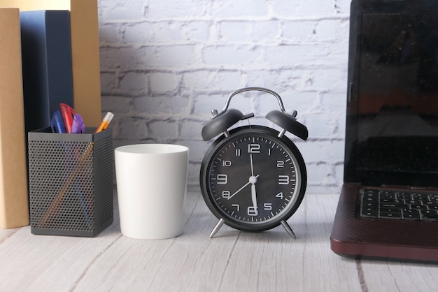 Pila de libros, portátil y reloj de mesa de cerca.