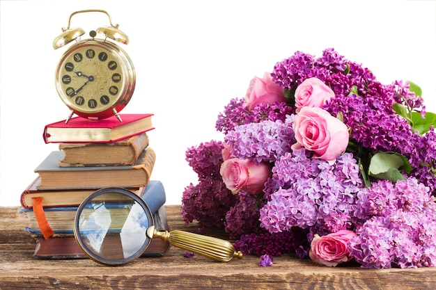 Pila de libros y reloj con flores lilas y rosas aisladas en blanco