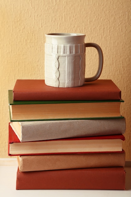 Pila de libros con una taza de bebida caliente sobre la mesa en la pared de luz