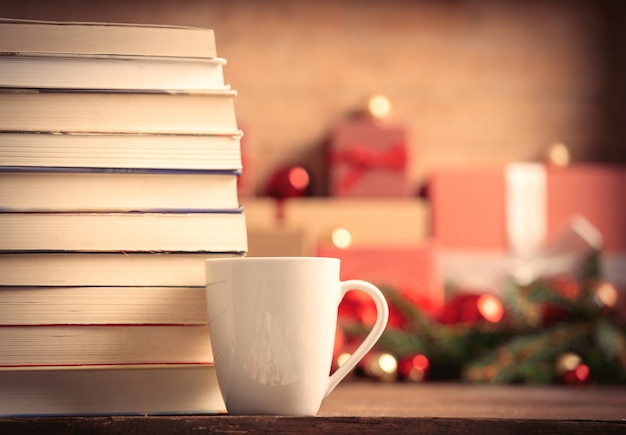 Pila de libros y una taza de café con regalos de Navidad en el fondo