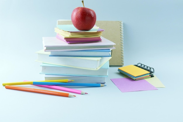 Una pila de libros de texto, lápices de colores, un cuaderno de bocetos y una manzana roja.