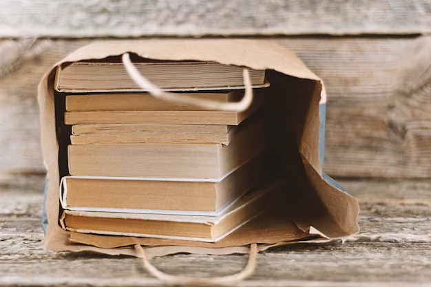 Pila de libros viejos en bolsa de papel sobre fondo de madera