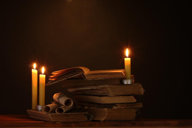 Pila de libros viejos con vela y pergamino en la oscuridad