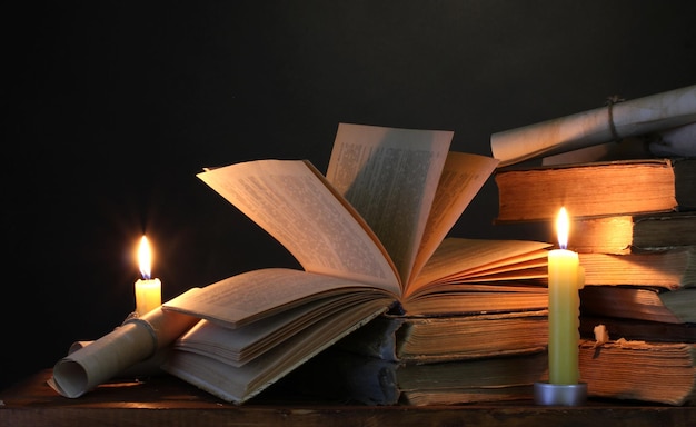 Pila de libros viejos con vela y pergamino en la oscuridad