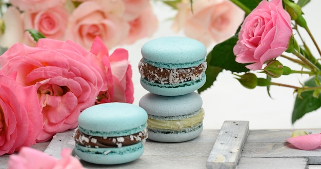 Pila de macarons azules sobre una mesa blanca y capullos de rosa rosa, delicioso postre, cerrar