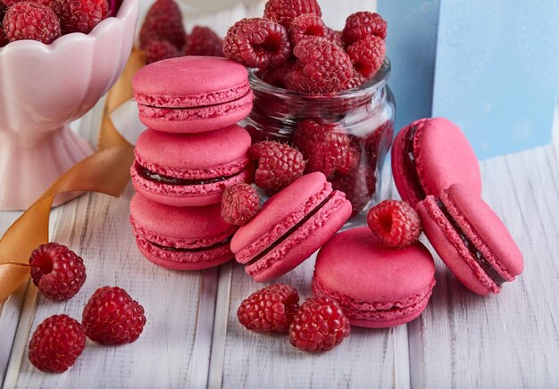 Una pila de macarrones rosados rodeados de frambuesas en una mesa de madera