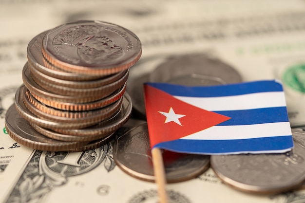 Pila de monedas con la bandera de Cuba sobre fondo de billetes de dólar estadounidense.
